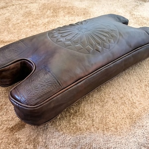 Side view of handmade camel stool cushion showing padded leather thickness, curved shape, and stitched edges for a custom replacement seat.