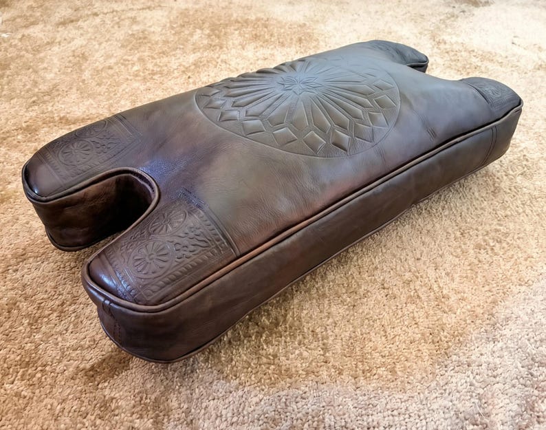 Side view of handmade camel stool cushion showing padded leather thickness, curved shape, and stitched edges for a custom replacement seat.