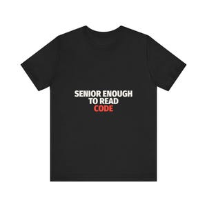 Könnte beinhalten: Ein schwarzes kurzärmeliges T-Shirt mit dem weißen Text SENIOR ENOUGH TO READ und dem roten Text CODE mittig auf der Brust. Das Kleidungsstück hat einen Rundhalsausschnitt und eine Standardpassform mit klarer, fetter Schrift auf dem Stoff.