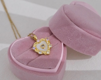 May include: A gold heart-shaped pendant necklace with a white mother-of-pearl center and colorful gemstones around the edge. The necklace is in a pink velvet heart-shaped box.