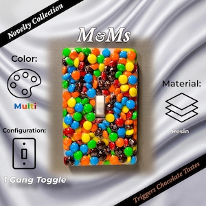 May include: A rectangular light switch cover featuring a 1-gang toggle configuration. The surface is embedded with numerous colorful, round chocolate candies in shades of red, yellow, green, blue, orange, and brown, encased in a clear resin finish.