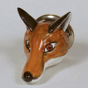 May include: A ceramic fox head wall mount with a brown and orange fur pattern, black eyes, and a white nose. The fox head is mounted on a silver base.