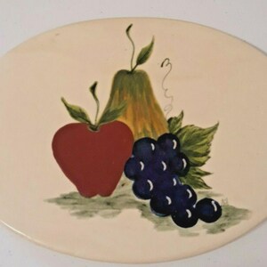 May include: Oval ceramic serving platter with a hand-painted fruit design. The design features a red apple, a yellow pear, and a cluster of dark blue grapes with green leaves. The platter has a cream-colored background.