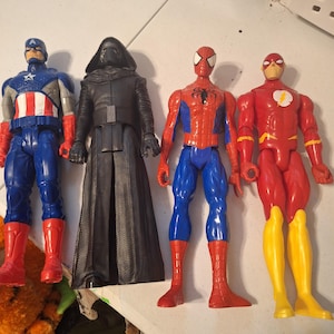Może przedstawiać: Cztery figurki akcji popularnych postaci z komiks&oacute;w i film&oacute;w. Kapitan Ameryka w kolorze niebieskim, czerwonym i białym. Kylo Ren w kolorze czarnym. Spider-Man w kolorze czerwono-niebieskim. Flash w kolorze czerwono-ż&oacute;łtym.