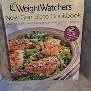 May include: A Weight Watchers cookbook titled "New Complete Cookbook" with a photo of a healthy meal on the cover. The cover also includes text about recipes and the Weight Watchers plan.