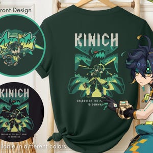 Pode incluir: Uma camiseta verde escura com um design pixelado que inclui o texto "KINICH" e a frase "SHADOW OF THE PAST, MINE TO COMMAND". O design também inclui uma criatura verde com uma expressão ameaçadora. Um personagem com cabelo azul e roupas verdes é mostrado no canto inferior direito da imagem.