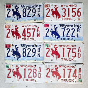 May include: Eight vintage Wyoming licence plates with a bucking bronco design. The plates are white with blue and red lettering and feature the state name "Wyoming" and the year of issue. The plates are numbered 2 829, 2 3156, 2 457, 2 722, 2 829, 2 175, 2 128, and 2 174.