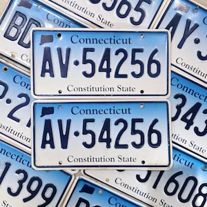 Op de afbeelding: Twee blauwe en witte kentekenplaten uit Connecticut met hetzelfde kentekennummer "AV-54256" en de tekst "Constitution State".