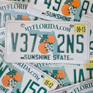 Puede incluir: Placa de matrícula blanca de Florida con letras verdes y un gráfico de fruta naranja. La placa dice "MYFLORIDA.COM" y "SUNSHINE STATE". Los números de la placa son V37 2NS. Una pegatina amarilla muestra la fecha 06-13.