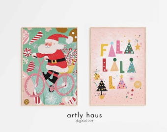 May include: Two rectangular wall art prints. The left print features Santa Claus riding a pink bicycle against a teal background with candy canes. The right print has a light pink background with the text FALA LALA LA and colorful Christmas trees.