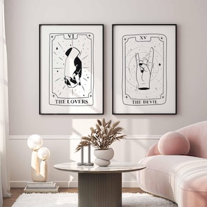 Puede incluir: Dos láminas de arte mural enmarcadas en blanco y negro con diseños de cartas del tarot. La lámina izquierda muestra dos manos entrelazadas con el texto VI y THE LOVERS. La derecha muestra una mano haciendo un gesto de rock con XV y THE DEVIL.