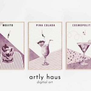 May include: Three framed wall art prints in shades of purple and white. The prints feature illustrations of a Mojito, a Pina Colada, and a Cosmopolitan cocktail, each with a small figure diving into the drink. The text artly haus digitial art appears below.
