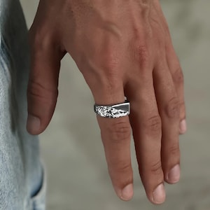 Könnte beinhalten: Ein silberner Ring mit einer strukturierten, unregelmäßigen Oberfläche. Der Ring wird am Zeigefinger einer Hand getragen.