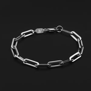 Könnte beinhalten: Silberfarbenes Kettengliederarmband mit Karabinerverschluss. Das Armband hat eine Reihe von länglichen, rechteckigen Gliedern. Der Verschluss hat ein kleines eingraviertes Design. Der Hintergrund ist schwarz.