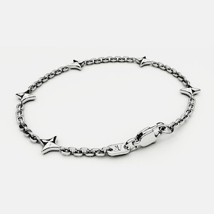 Könnte beinhalten: Ein silberfarbenes Armband mit einem Kettenmuster und sternförmigen Anhängern. Das Armband hat einen sicheren Verschluss. Der Schmuck wird vor einem schlichten weißen Hintergrund präsentiert. Das Metall glänzt.