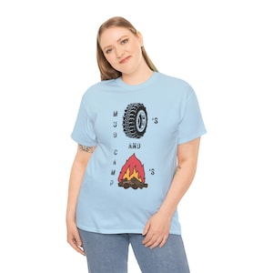 May include: Light blue t-shirt with the text "MUD AND CAMP'S" and graphics of a tire and a campfire. The tire is black and white, and the campfire is red, orange, and yellow.