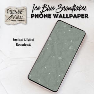May include: A smartphone displays an ice blue snowflake phone wallpaper. The wallpaper has a textured, crumpled paper effect with white snowflakes and diamond shapes. The phone is angled, showing the screen and a rose gold frame. Text on the image reads "Ice Blue Snowflakes PHONE WALLPAPER".