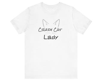 May include: White t-shirt with a black graphic of a cat's face and the words "Crazy Cat Lady" in a handwritten style font. The shirt is made of a soft material and has a crew neck.