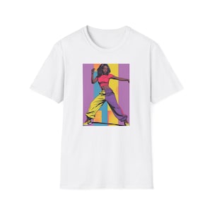 Puede incluir: Camiseta blanca con una ilustración de estilo pop art de una persona en una pose dinámica. La persona lleva un top corto rojo y pantalones de bloques de color amarillos y morados. El fondo tiene rayas verticales.