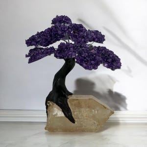 Pode incluir: Uma escultura decorativa de árvore bonsai com um tronco escuro e curvo e uma copa de cristais de ametista roxos profundos. A árvore é montada em uma grande base de cristal de quartzo transparente, criando um contraste marcante.