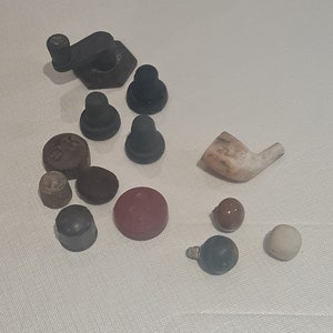 Puede incluir: Surtido de objetos pequeños, redondos y de formas extrañas en varios colores, incluyendo negro, marrón, rojo, blanco y beige. Algunos objetos tienen una superficie lisa, mientras que otros tienen una superficie texturizada. Los objetos están dispuestos sobre una superficie blanca.