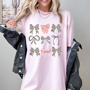 Puede incluir: Camiseta rosa claro con un dise&ntilde;o de nueve lazos de varios estilos. Los lazos incluyen estampado de leopardo, rosa liso y verde oliva. La camiseta tiene un corte holgado y cuello redondo.