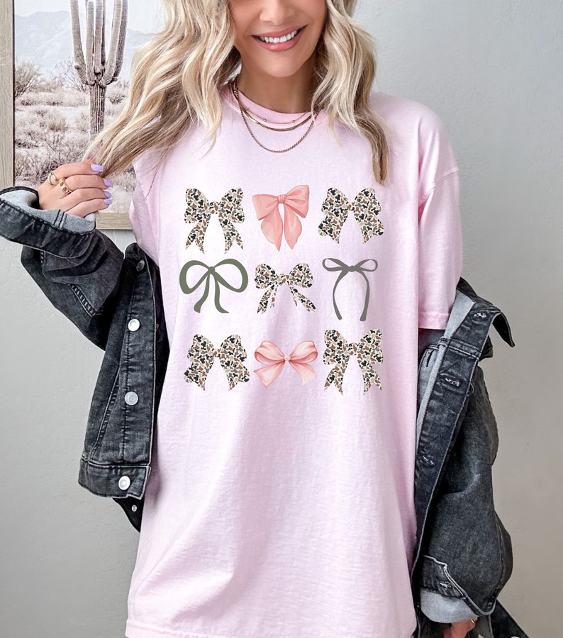 Puede incluir: Camiseta rosa claro con un dise&ntilde;o de nueve lazos de varios estilos. Los lazos incluyen estampado de leopardo, rosa liso y verde oliva. La camiseta tiene un corte holgado y cuello redondo.