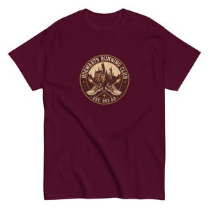 May include: A maroon t-shirt featuring a circular graphic for the "Hogwarts Running Club." The design includes crossed running shoes, a castle silhouette, and the text "EST. 993 AD."