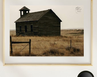 May include: A weathered wooden building with a bell tower stands alone in a field of tall grass. A barbed wire fence runs in front of the building. The image is in sepia tones.