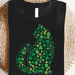 May include: Black t-shirt with a green cat silhouette made of shamrocks. The cat is sitting with its tail curled around its body.