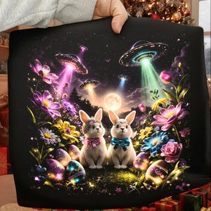 May include: A black pillowcase featuring a whimsical scene with two bunnies, UFOs, and colorful flowers under a starry night sky. The bunnies wear floral crowns and bow ties, surrounded by decorated Easter eggs.