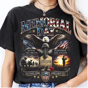May include: Black t-shirt with a patriotic Memorial Day design. Features an eagle, American flags, and text that reads "Memorial Day", "Honor the Brave", "Remember the Fallen", "Freedom", "All Gave Some", and "Some Gave All".