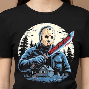 May include: Black t-shirt featuring a graphic of a masked figure holding a bloody machete with the text "FRIDAY THE 13TH". The design includes a cabin in the woods and a forest backdrop.