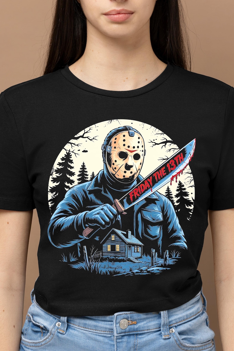 May include: Black t-shirt featuring a graphic of a masked figure holding a bloody machete with the text "FRIDAY THE 13TH". The design includes a cabin in the woods and a forest backdrop.
