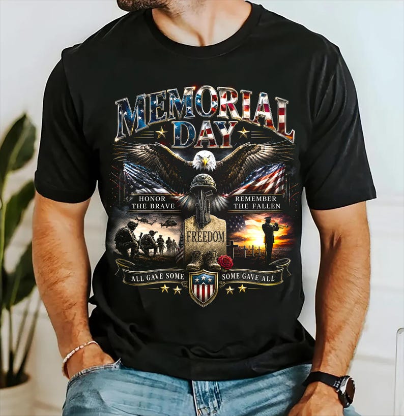 May include: Black t-shirt with a Memorial Day graphic. The design features an eagle, American flags, and the text "Memorial Day." Additional text includes "Honor the Brave," "Remember the Fallen," and "Freedom."
