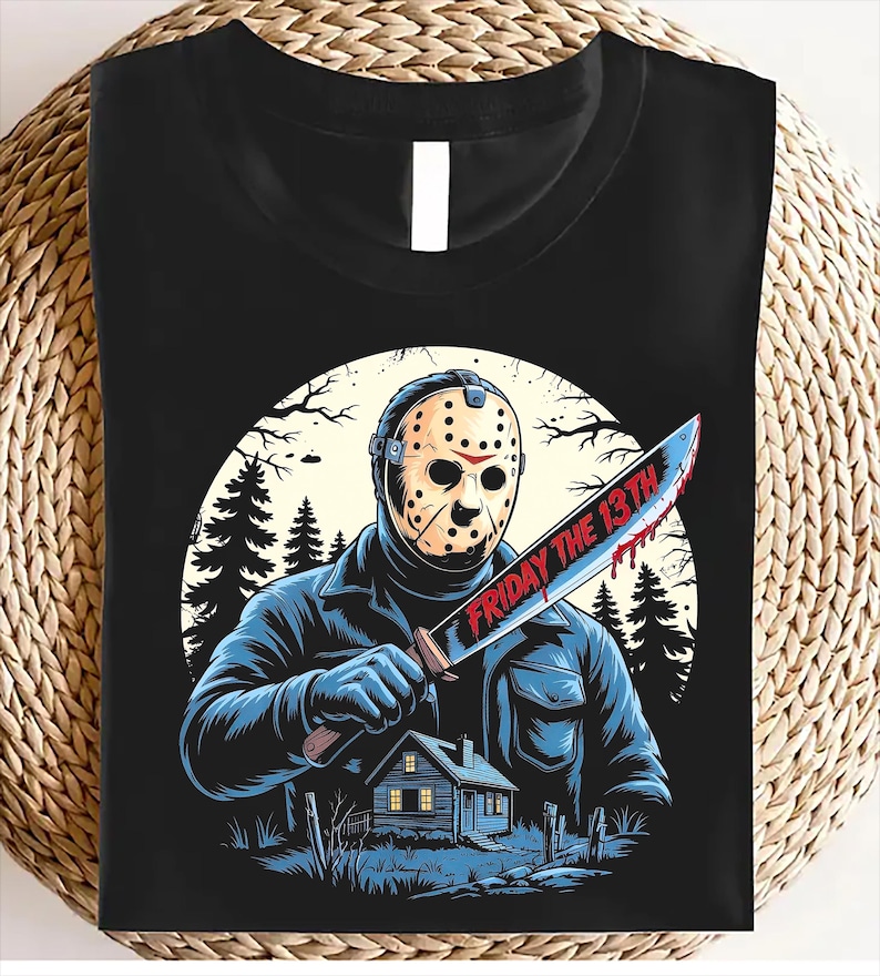 May include: Black t-shirt featuring a graphic of a masked figure holding a bloody knife with the text "FRIDAY THE 13TH". The design includes a cabin, trees, and a full moon, creating a horror movie theme.
