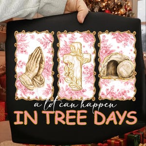 Op de afbeelding: Zwarte draagtas met drie ingelijste afbeeldingen met gouden randen. De afbeeldingen tonen biddende handen, een kruis en een leeg graf. De tekst "a lot can happen IN TREE DAYS" is in roze geschreven.