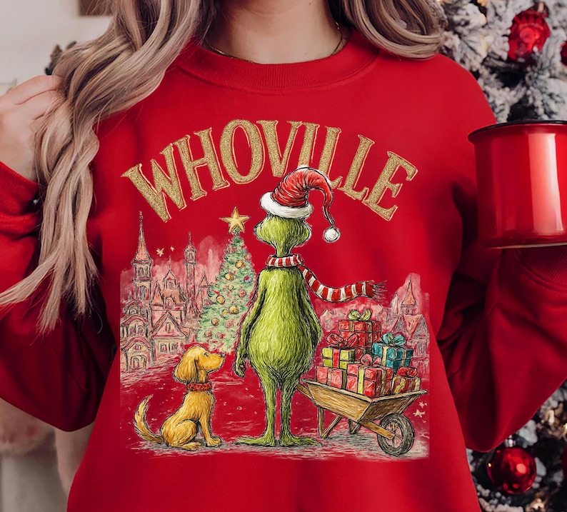 May include: Red sweatshirt featuring a graphic of the Grinch in a Santa hat and scarf, with a dog and a cart of gifts. The word "Whoville" is printed above the Grinch in gold lettering. A Christmas tree and buildings are in the background.