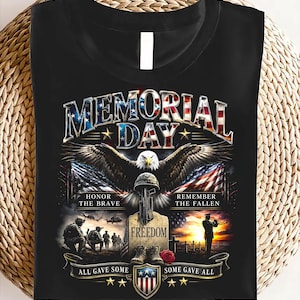 May include: Black t-shirt with a Memorial Day graphic. The design features an eagle, American flags, and the text "Memorial Day", "Honor the Brave", "Remember the Fallen", "Freedom", "All Gave Some", and "Some Gave All".