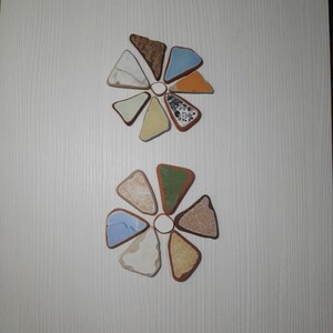 May include: Two sets of triangular tiles arranged in a flower shape. The tiles are in various colours and patterns, including brown, orange, blue, green, white, and black.
