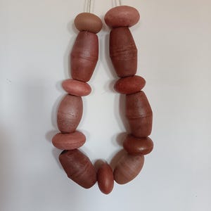 Pode incluir: Um fio de contas de terracota, cada uma com uma forma e textura ligeiramente diferentes, penduradas em um fio branco.