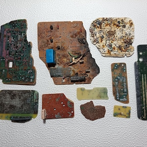 May include: A selection of damaged circuit boards, displaying a range of colours and forms. The boards feature green, brown, and yellow hues, with visible electronic parts. Some boards have a blue component. The image is taken from above.