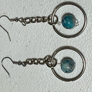 May include: A pair of silver earrings with a blue and white agate bead on each earring. The beads are attached to a silver chain and a silver hoop.