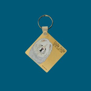 May include: A white Chow Chow dog with a fluffy coat is featured on a yellow square keyring with the text "Chow Chow or the floor, please".