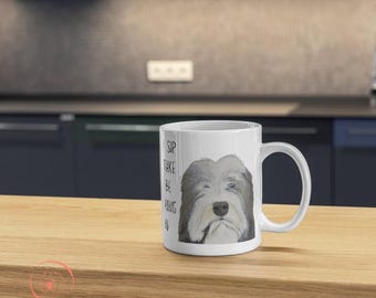 May include: White ceramic mug with a black and white illustration of a Bearded Collie dog. The mug has the text "Sip, Take, Be, Hang, By" printed on it.