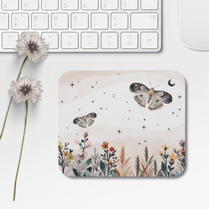 May include: A mouse pad with a watercolor design featuring butterflies, stars, and a crescent moon. The background is a soft beige with a subtle watercolor effect. The butterflies are a light blue and gray with black accents. The stars are white and the crescent moon is a light gray.