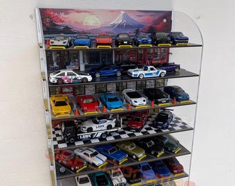 May include: A clear acrylic display case with 7 shelves holds a collection of miniature toy cars. The cars are arranged in rows and are mostly red, blue, yellow, and white. The back of the case features a printed image of a Japanese mountain scene.