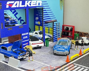 May include: A miniature toy garage with a blue and white Falken sign, a blue car on a lift, and a blue car with a Mazda logo being worked on by a miniature figure.