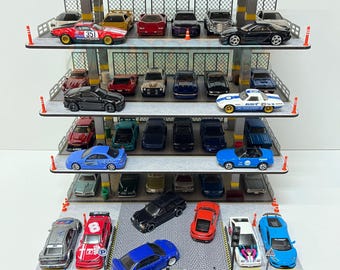 Może przedstawiać: Model garażu dla zabawek wypełniony miniaturowymi samochodzikami. Samochody są w różnych kolorach i stylach, w tym samochody sportowe i sedany. Garaż ma wiele poziomów, z szaro-czarną kolorystyką. Samochody są rozmieszczone na poziomach.