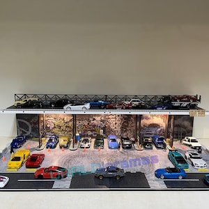 May include: A model car garage display with a variety of colorful cars, including red, blue, yellow, and white. The garage has a graffiti-style wall with the words "Eat Sleep Street" on it.